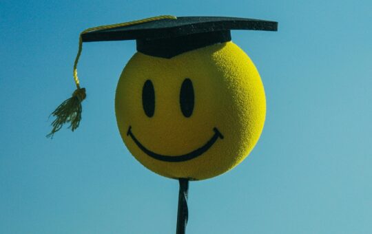 A smiley face wearing a graduation cap illustrating Carl by the Autoscience Institute, the first AI system crafting academic research papers to pass a rigorous double-blind peer-review process and raising questions about ethics including the role of artificial intelligence in academic settings.